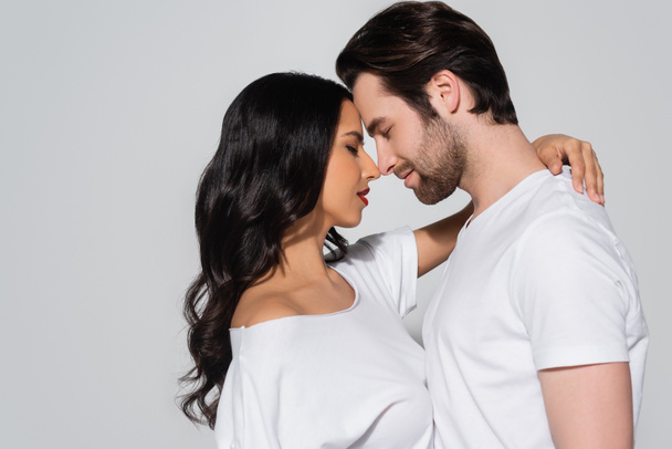 side view of brunette woman embracing man while standing face to face with closed eyes isolated on grey - Photo, Image