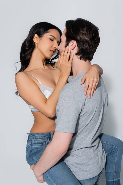 mulher apaixonada em sutiã e jeans beijando o homem em t-shirt em cinza - Foto, Imagem