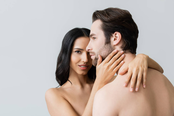 mujer desnuda mirando a la cámara mientras abraza hombre sin camisa aislado en gris - Foto, imagen