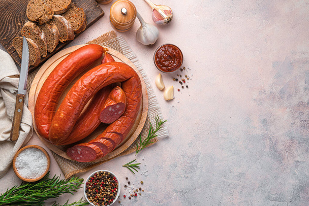 Smoked, spicy sausage with spices, sauce and bread on a light background. Top view, copy space. - Photo, Image