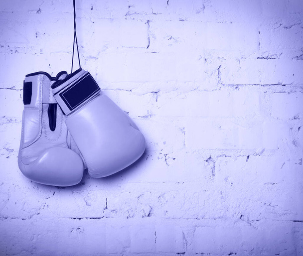 Пара жёлтых боксерских перчаток, висящих на кирпичной стене. Цвет 2022 года, очень пери, тонированный - Фото, изображение