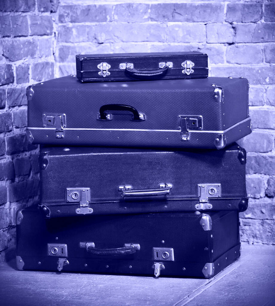 Старые винтажные чемоданы, изолированные возле кирпичной стены. Багаж. Цвет 2022 года, очень пери, фиолетовый - Фото, изображение