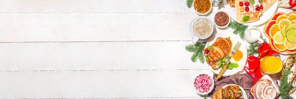 Χριστουγεννιάτικο πρωινό ή brunch table, με παραδοσιακά φαγητά τηγανίτες, βελγικές βάφλες, τηγανητά αυγά, κρουασάν, κλεμμένα, μπισκότα, με χυμό πορτοκαλιού και καφέ, κανέλα ρύζι χυλό - Φωτογραφία, εικόνα