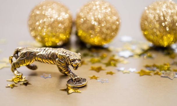 Eine Bronzefigur eines Tigers mit einer Münze - das Symbol des chinesischen Neujahrs 2022 auf einem Hintergrund aus Sternen, goldglänzenden Kugeln, Kopierraum. Wünsche nach Glück, finanziellem Wohlergehen und Wohlstand. - Foto, Bild