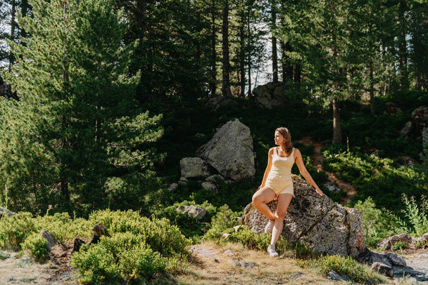 Pretty young girl in the yellow T-shirt and yellow shorts sitting on the stone above the beautiful canyon. Traveler in the mountains. Hipster girl in the mountains. Stylish woman in checkered shirt - Fotografie, Obrázek