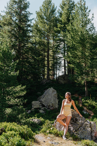 Young woman tourist sitting on the mountain peak and beautiful mountains. Landscape with sporty girl, green forest, hills , sky, lake. Travel and tourism. Hipster girl in the mountains. Stylish woman - Fotografie, Obrázek