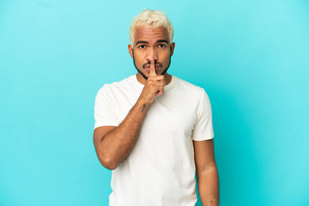 Young Colombian handsome man isolated on blue background showing a sign of silence gesture putting finger in mouth - Fotografie, Obrázek