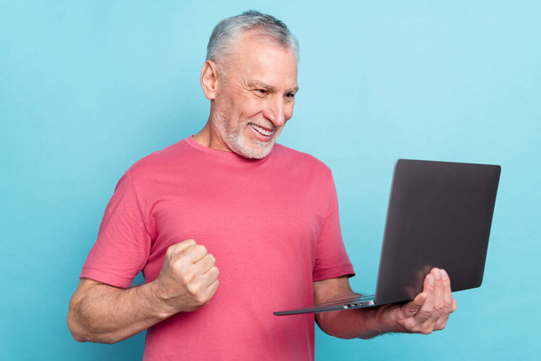 Photo portrait elder man smiling using laptop browsing internet gesturing like winner isolated pastel blue color background - Foto, Bild