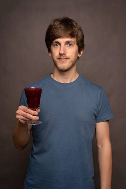 Young handsome tall slim white man with brown hair holding wine cup in grey shirt on grey background - Φωτογραφία, εικόνα