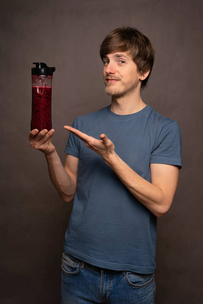 Young handsome tall slim white man with brown hair presenting smoothie bottle in grey shirt on grey background - Foto, immagini