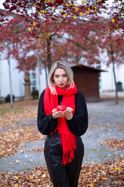 European white young woman with blonde hair in red scarf holding a red apple in autumn - Fotó, kép