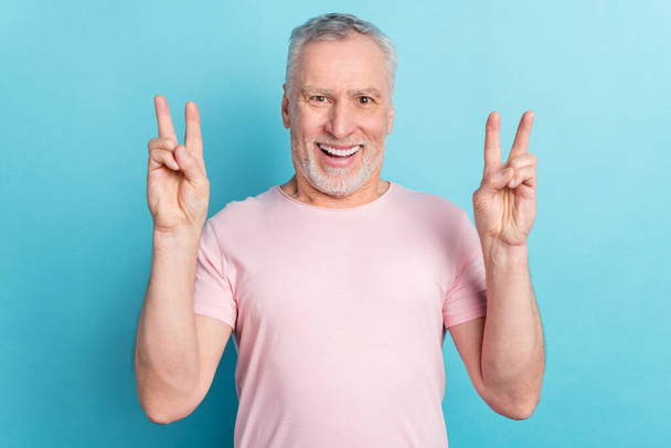 Photo portrait smiling elder man in pink t-shirt showing v-sign gesture isolated on pastel blue color background - Foto, afbeelding