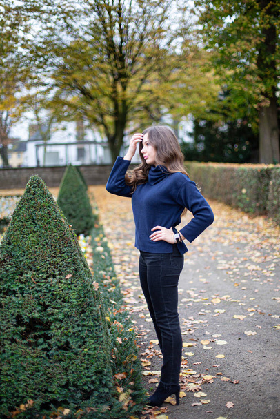 Young european woman in dark blue jumper with long curly hair in autumn park holding hand near forehead - Φωτογραφία, εικόνα