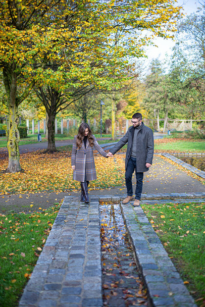 White young man and woman holding hands in autumn park - Foto, afbeelding