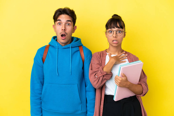 Молодая студенческая пара изолирована на желтом фоне с удивлением и шокированным выражением лица - Фото, изображение