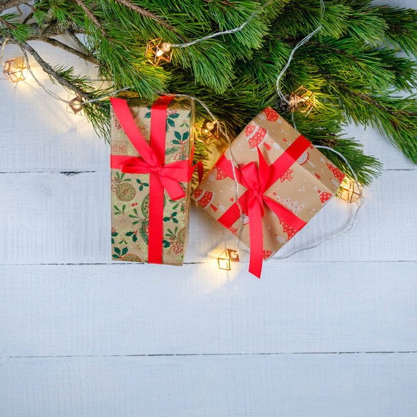Caixas de presente de Natal em fundo de madeira branca com ramo de árvore de Natal e luzes. Tema de Natal e Feliz Ano Novo. Deitado plano, vista superior. Espaço de cópia - Foto, Imagem