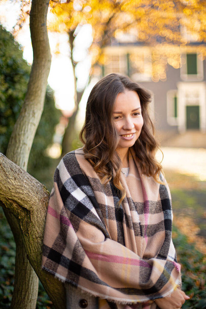 Pretty young woman with brown curly hair in warm scarf in autumn park - Foto, Imagen