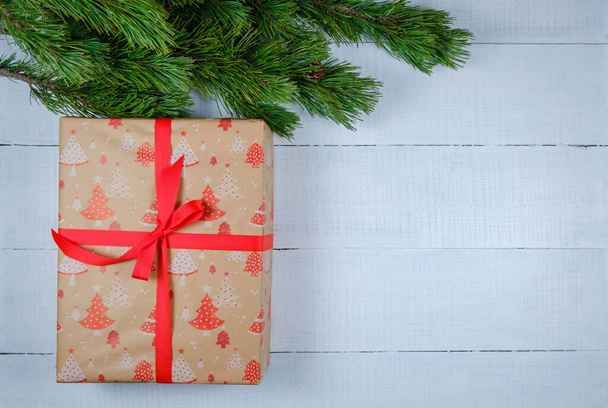 Χριστουγεννιάτικο κουτί δώρου σε λευκό ξύλινο φόντο με κλαδί χριστουγεννιάτικου δέντρου. Χριστούγεννα και Καλή Χρονιά. Επίπεδη θέα. Αντιγραφή χώρου - Φωτογραφία, εικόνα