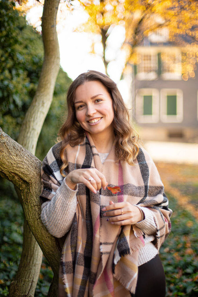 Smiling young woman with brown curly hair in warm scarf in autumn park - Fotó, kép