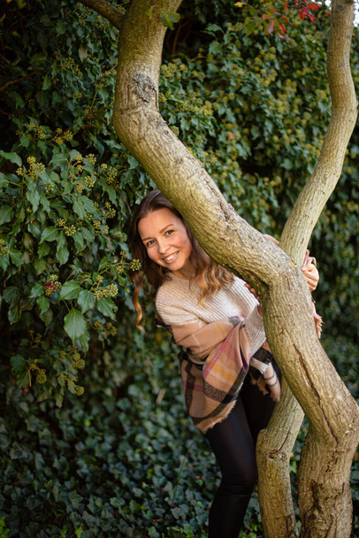 Hiding european white young woman with brown hair near tree trunk with bushes behind - Zdjęcie, obraz