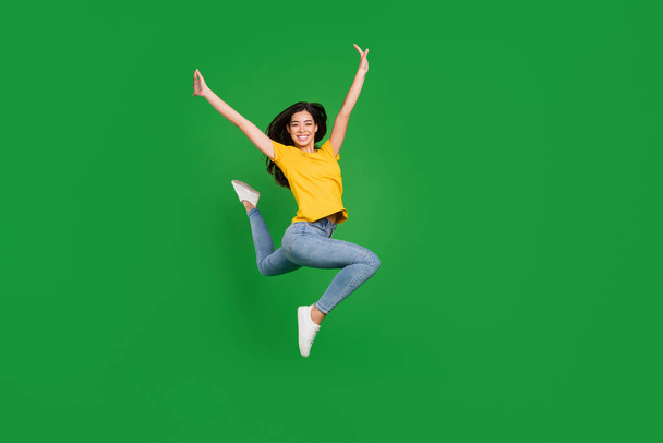 Full size photo of cheerful nice young woman jump up raise hands good mood smile isolated on green color background - Zdjęcie, obraz