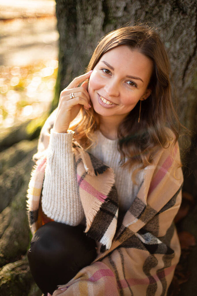 Portrait of european young white woman with brown hair with warm autumn scarf near the tree - Фото, изображение