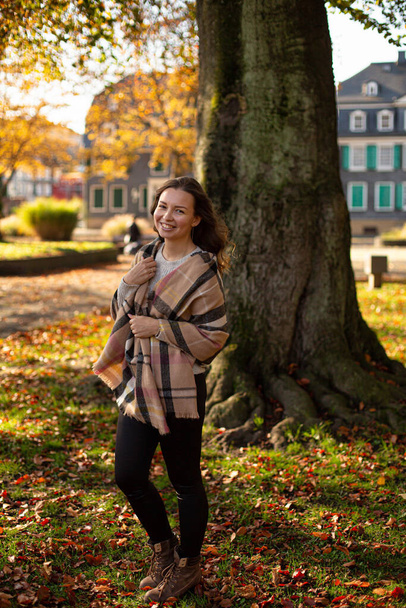 White young european woman with brown hair with warm autumn scarf with trees behind - Foto, afbeelding