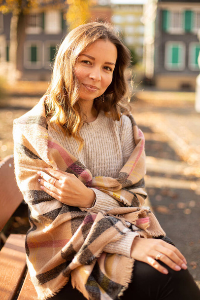 Smiling european white young woman with brown hair sitting on bench in sunny autumn - Foto, Imagen