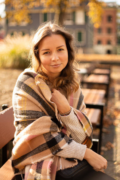 Smiling white young european woman with brown hair sitting on bench in sunny autumn - Foto, afbeelding