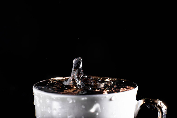 A drop of water falls into a cup on a black background. Splash on the water surface. - Photo, image