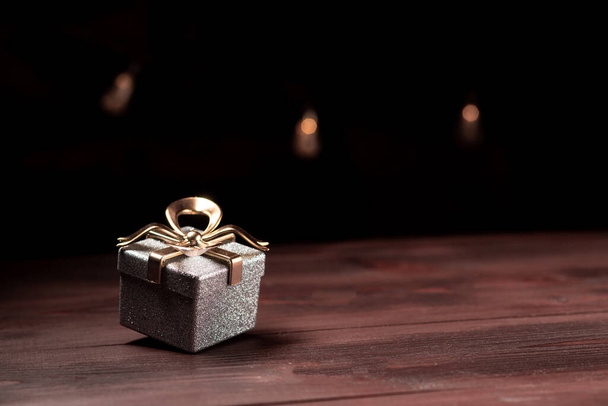 Concepto de regalo de año nuevo. Una caja brillante con un lazo sobre un fondo oscuro con luces de colores en el fondo. - Foto, imagen