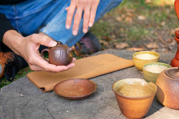 White man holding handmade ceramic tea pot with tea set on stump in city park - Valokuva, kuva