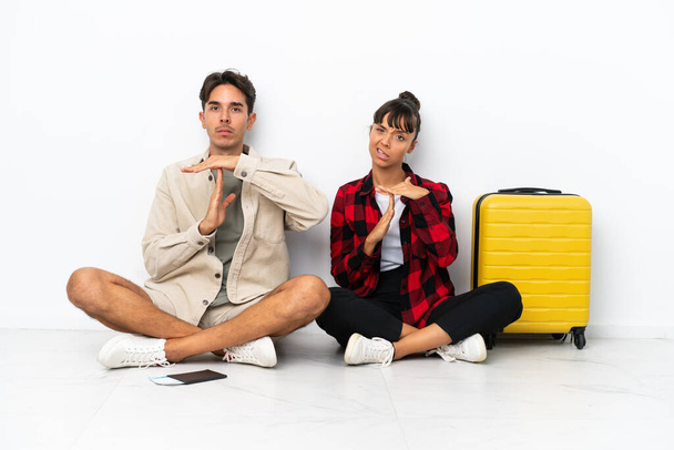 Молода змішана пара мандрівників, що сидять на підлозі ізольовані на білому тлі, роблять стоп жест рукою, щоб зупинити акт
 - Фото, зображення