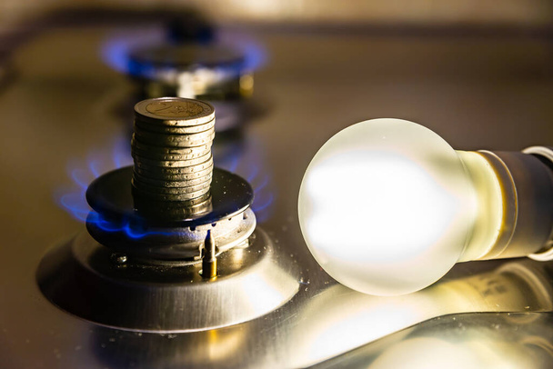 Light bulb on next to lit gas cooker, with coins next to it. Energy and gas costs, cost increases.Light bulb on next to lit gas cooker, with coins next to it. Energy and gas costs, cost increases. - Photo, Image