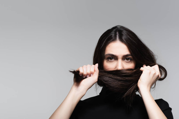 young woman covering mouth with brown hair isolated on grey - Фото, зображення