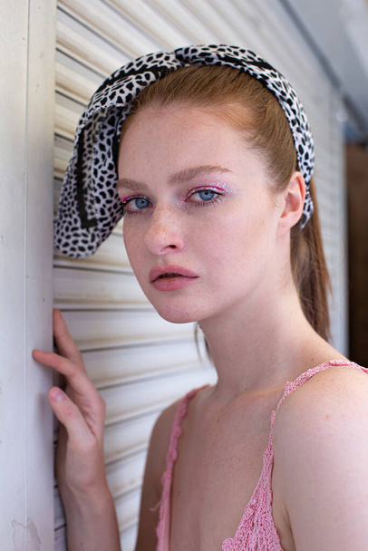 Portrait of white blond young woman with a ponytail in pink with blue eyes near the wall - Fotografie, Obrázek