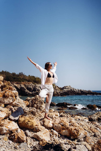 Traveler woman enjoys her vacation on sea coast practicing yoga - Photo, Image