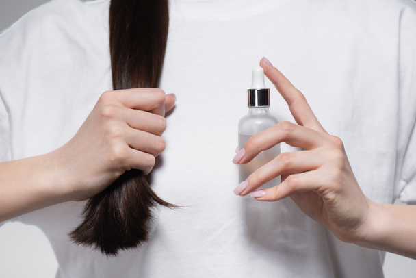 vista cortada de jovem segurando garrafa com óleo perto de cabelo brilhante  - Foto, Imagem
