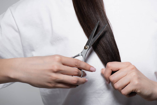 cropped view of woman in white t-shirt holding scissors near shiny hair isolated on grey - Фото, зображення