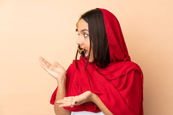 Young Indian woman isolated on beige background with surprise expression while looking side - Photo, Image