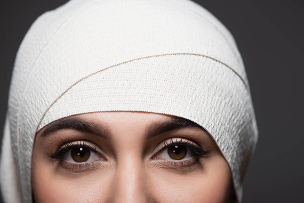 przycięty widok młodej kobiety w elastycznym bandażu na głowie patrząc na kamerę odizolowaną na szaro - Zdjęcie, obraz