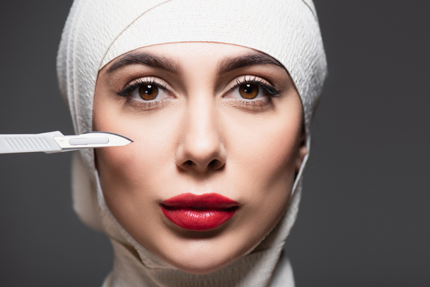 close up of woman in elastic bandage on head near sharp surgical knife isolated on grey  - Fotoğraf, Görsel