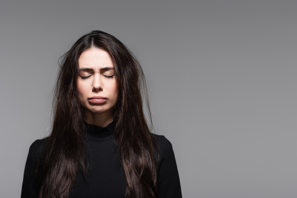 smutná mladá žena v černém roláku s poškozenými vlasy izolované na šedé  - Fotografie, Obrázek