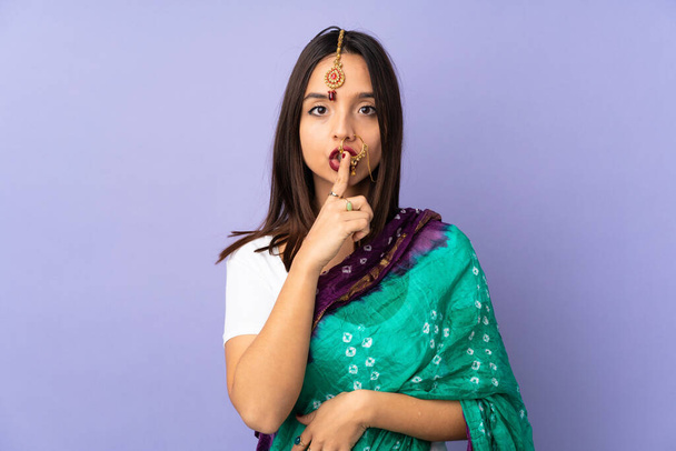 Young Indian woman isolated on purple background showing a sign of silence gesture putting finger in mouth - Fotó, kép