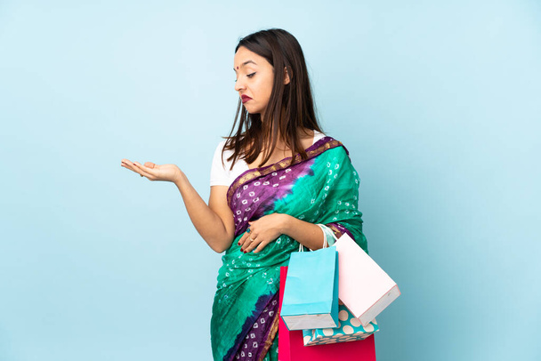 Νεαρή Ινδή γυναίκα με τσάντες για ψώνια κρατώντας copyspace με αμφιβολίες - Φωτογραφία, εικόνα