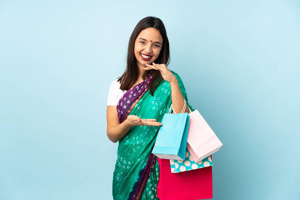 Junge Inderin mit Einkaufstaschen, die imaginären Kopierraum auf der Handfläche halten, um eine Anzeige zu schalten - Foto, Bild
