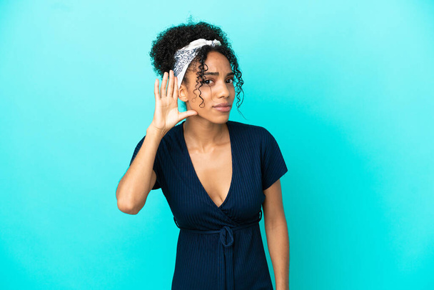 Young latin woman isolated on blue background listening to something by putting hand on the ear - Photo, image