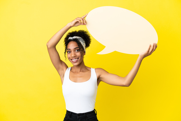 Молода афроамериканська жінка ізольована на жовтому фоні з порожньою бульбашкою мови. - Фото, зображення