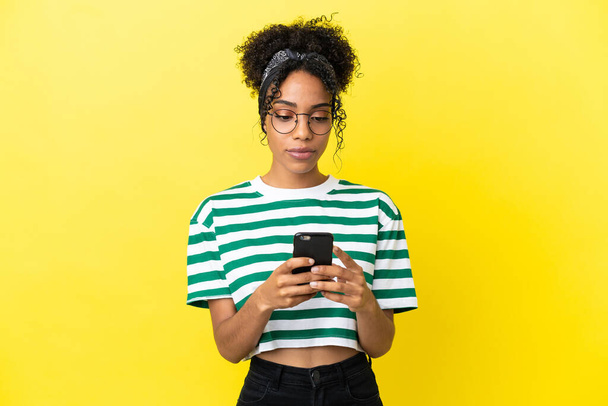 Young african american woman isolated on yellow background using mobile phone - Фото, изображение