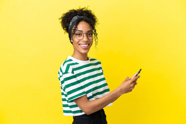 Young african american woman isolated on yellow background sending a message or email with the mobile - Фото, зображення